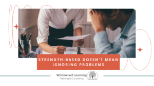 Two people sit at a table with papers; one person is handing a document to the other, who looks stressed. Text reads: Strength-based doesn’t mean ignoring problems. Wildewood Learning Training & Consulting.