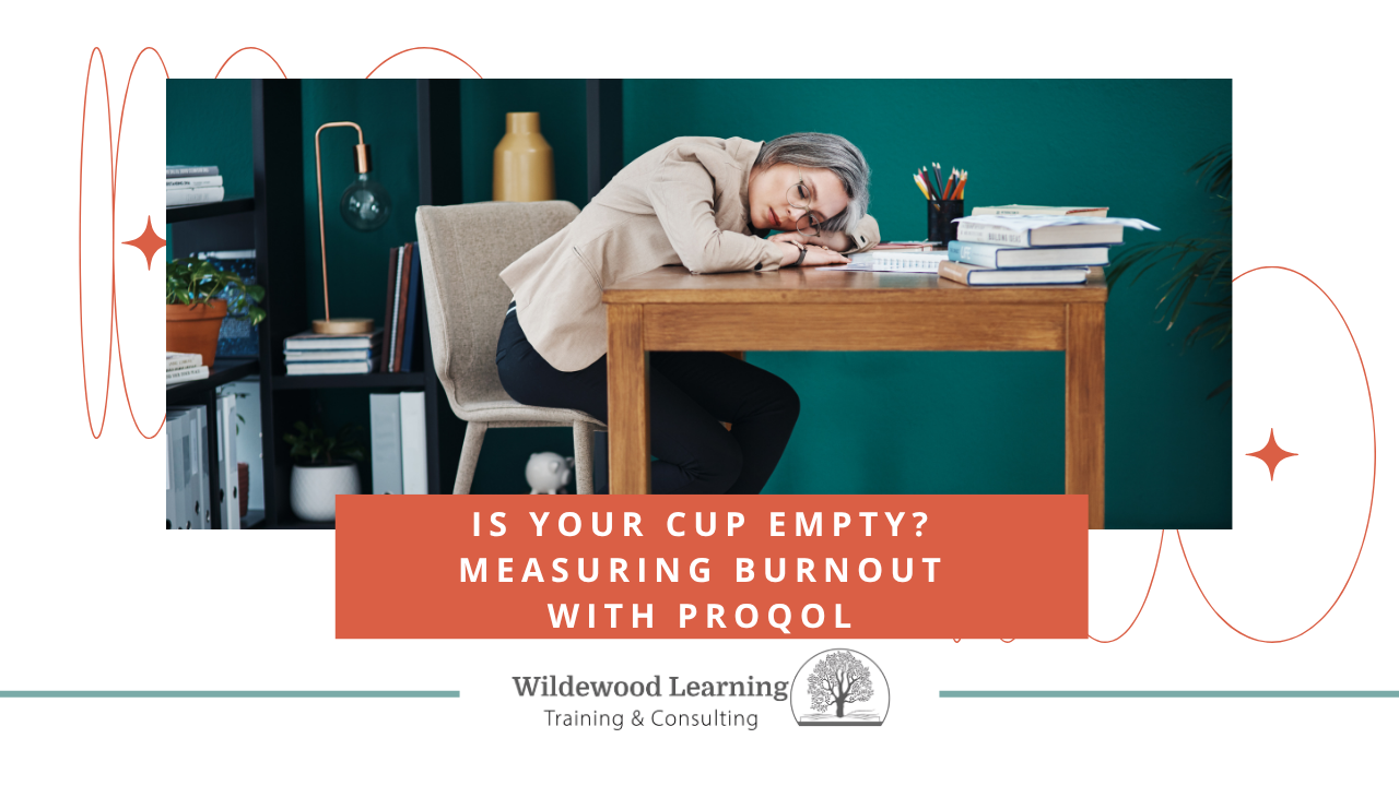 A woman leans tiredly on a desk cluttered with books and papers. Text overlay: Is your cup empty? Measuring burnout with ProQOL. Wildewood Learning Training & Consulting logo appears below.