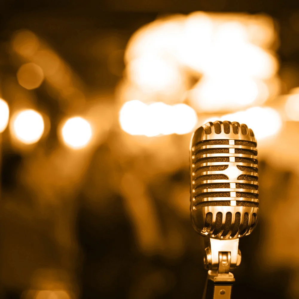 A vintage microphone in sharp focus stands in front of blurred, warm-toned lights, creating a nostalgic atmosphere.